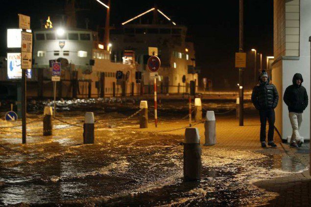 People walk past a flooded street at the harbour in Norddeich, December 5, 2013. Hurricane-force Storm Xaver blasted towards mainland Europe on Thursday after cutting transport and power in northern Britain and killing three people in what meteorologists warned could be the worst storm to hit the continent in years. REUTERS/Ina Fassbender