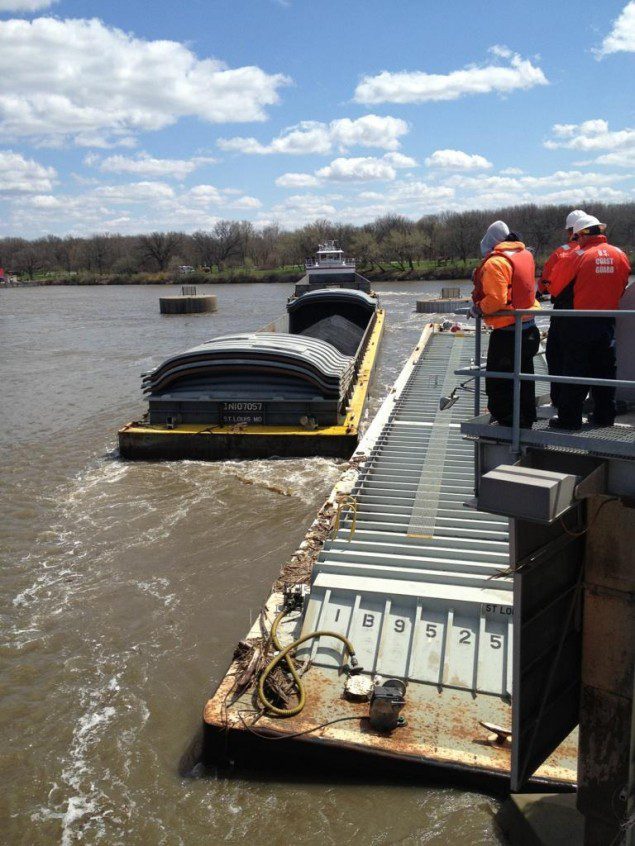 Members of the Unified Command watch as one of three additional barges is removed from near the Marseilles Dam in Marseilles, ill., during continued salvage operations, April 25, 2015. 