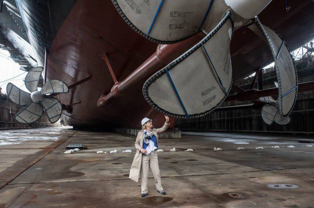Ship's sponsor Susan Ford Bales, President Ford's daughter, tries to spin one of the ship's giant propellers during a tour of the ship before the dry dock flooding. Photo by Chris Oxley, Huntington Ingalls Industries 