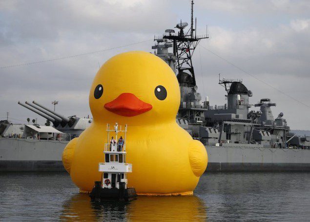 Giant inflatable rubber duck installation by Dutch artist Florentijn Hofman floats past the Battleship Iowa through the Port of Los Angeles as part of the Tall Ships Festival, in San Pedro