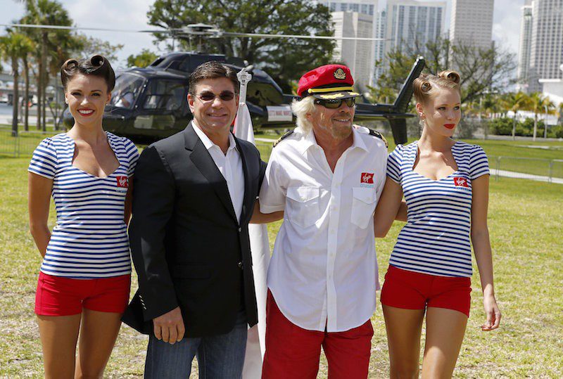 Richard Branson stands with Virgin Cruises' President and CEO Tom McAlpin as he arrives by helicopter for a news conference at the Perez Art Museum in Miami, Florida June 23, 2015. Branson’s London-based Virgin Group is launching a cruise line with two, custom-designed ships the company announced on Tuesday. The Virgin Group, which already has an airline and space tourism businesses, is partnering with private investment firm Bain Capital for the cruise line. REUTERS/Joe Skipper