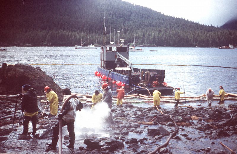 Cleanup workers steam blast rocks and washdown shorelines soaked in crude oil from the leaking tanker Exxon Valdez. The Exxon Valdez ran aground on Bligh Reef in Prince William Sound, Alaska, March 23, 1989 spilling 11 million gallons of crude oil, which resulted in the largest oil spill in U.S. history. U.S. Coast Guard Photo