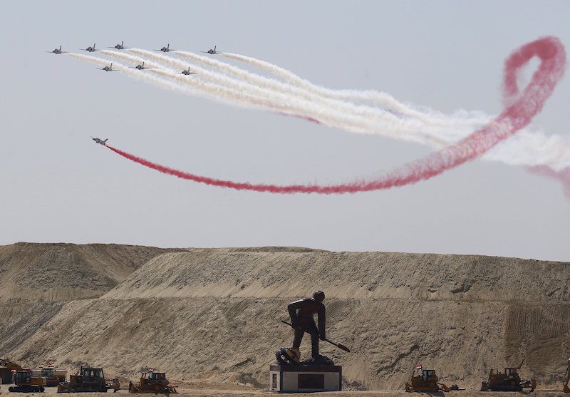 Egyptian air force planes parade in front of a statue representing a man digging during the inauguration ceremony of the new Suez Canal, in Ismailia