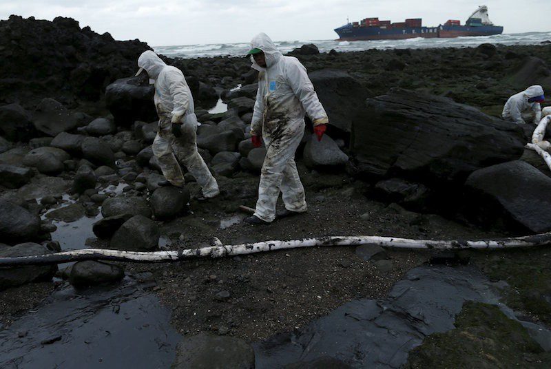 Cleaners walk past protective booms around fuel that leaked from a cargo ship owned by TS Lines Co (in background), off the shores of New Taipei City, Taiwan, March 25, 2016. Photo: REUTERS/Tyrone Siu