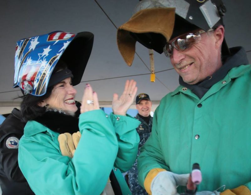 Luci Baines Johnson applauds Timothy Trask, a Bath Iron Works welder, after he helped her authenticate the keel plate of DDG 1002, the future USS Lyndon B. Johnson, January 30, 2017. Photo: Bath Iron Works
