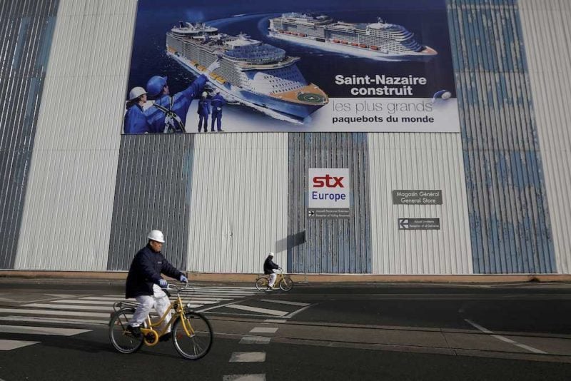 FILE PHOTO Shipbuilders ride past a giant poster November 9, 2016 at the STX Les Chantiers de l'Atlantique shipyard site in Saint-Nazaire, western France. REUTERS/Stephane Mahe/File Photo