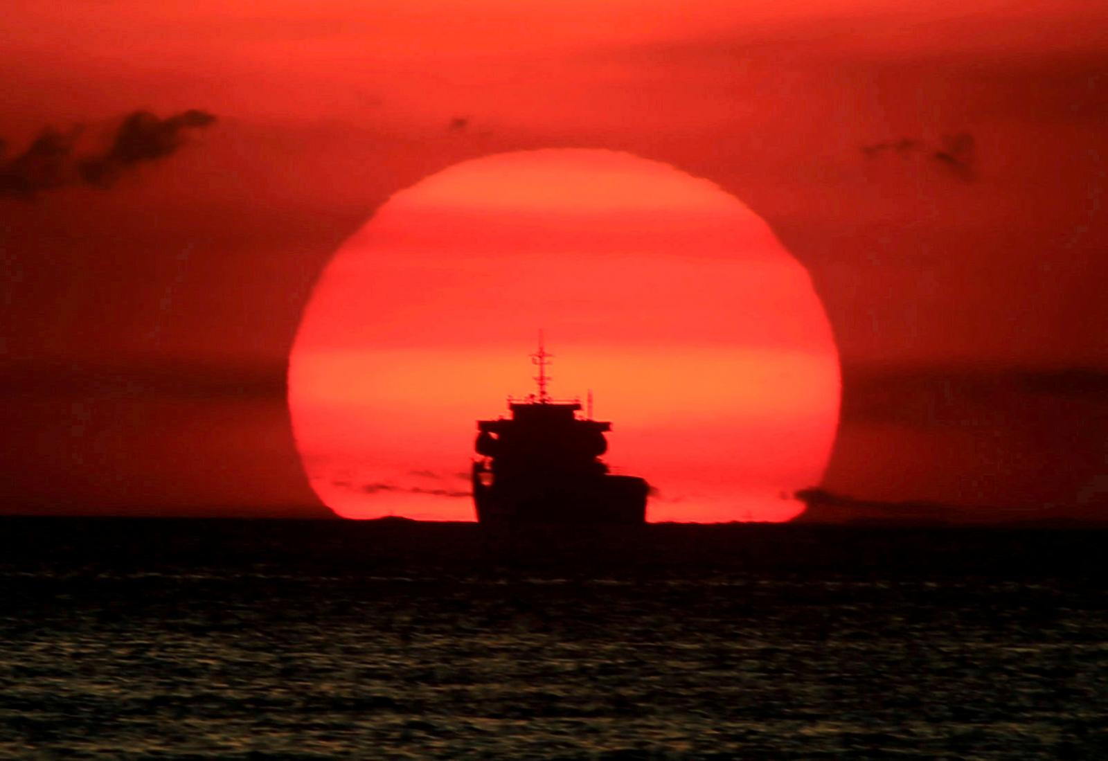 A cargo ship is silhouetted as the sun sets along the coast of Manila bay