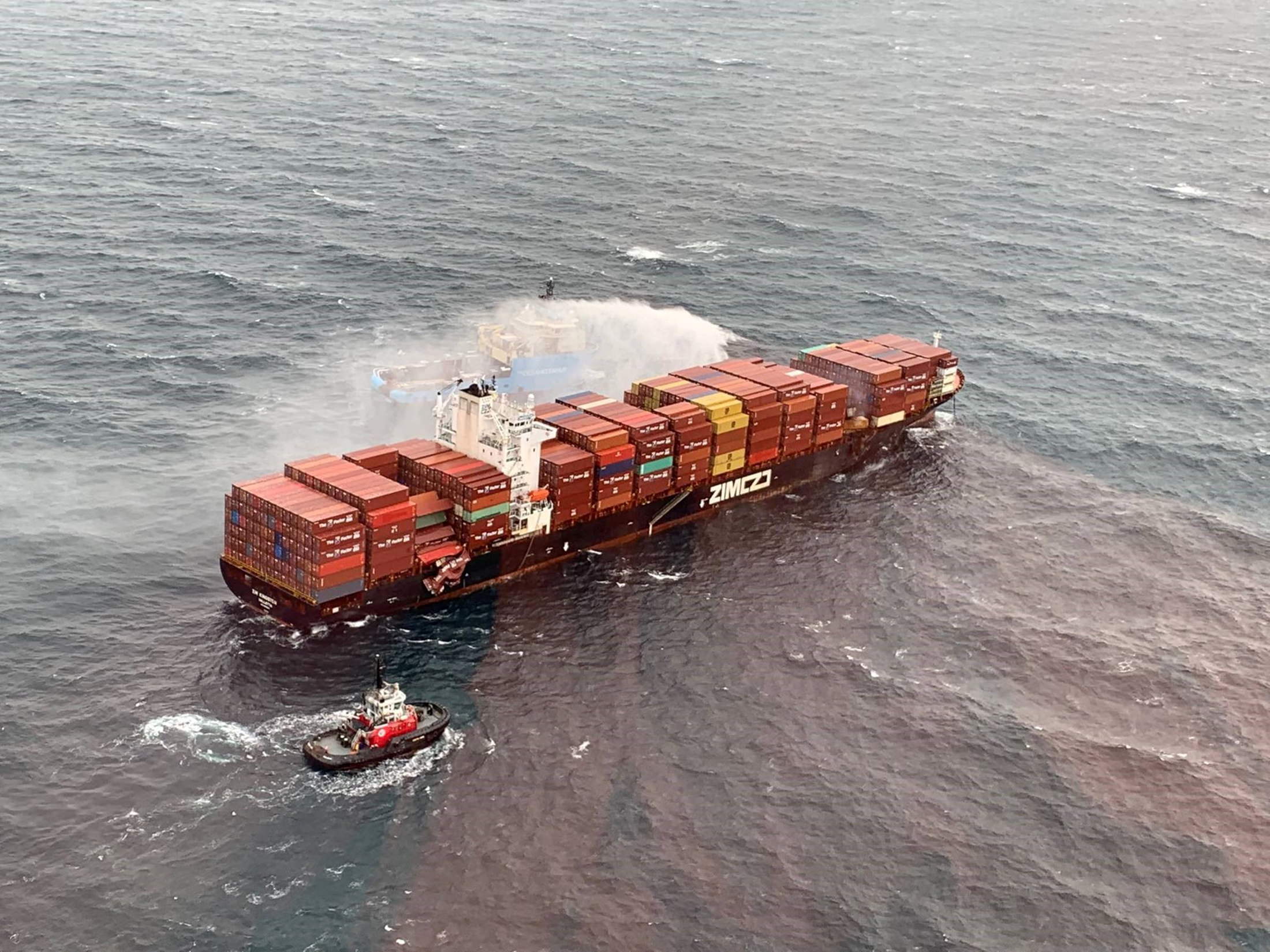 A tugboat pours water on the container ship Zim Kingston after it caught fire off the coast of Victoria, British Columbia, Canada October 25, 2021. Canadian Coast Guard/Handout via REUTERS