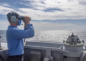 A U.S. Navy sailor looks through binoculars on the bridge as the Arleigh Burke-class guided-missile destroyer USS Mustin (DDG 89) during routine operations in the Taiwan Strait, August 18, 2020.