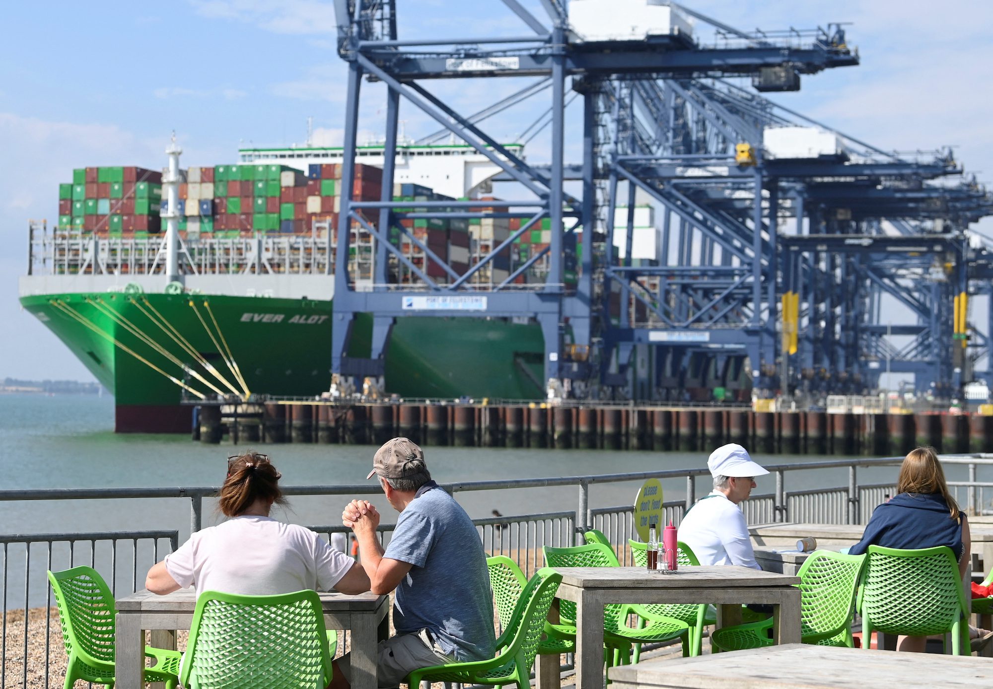 People sit at a beach cafe with the Britain's biggest container port Felixstowe seen behind