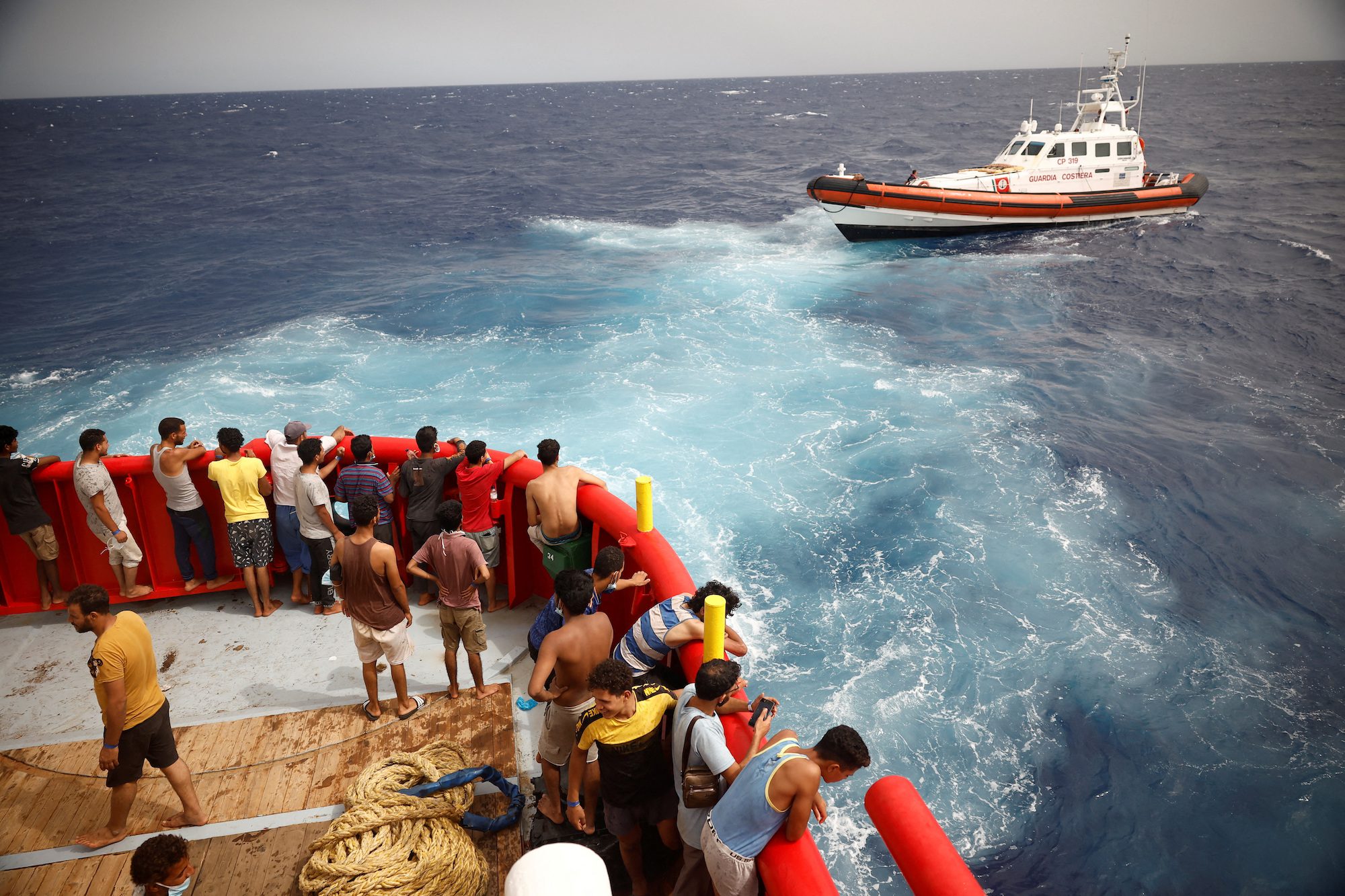 Migrants on board of NGO Proactiva Open Arms Uno rescue boat looks at boat Guardia Costiera heading to Lampedusa island