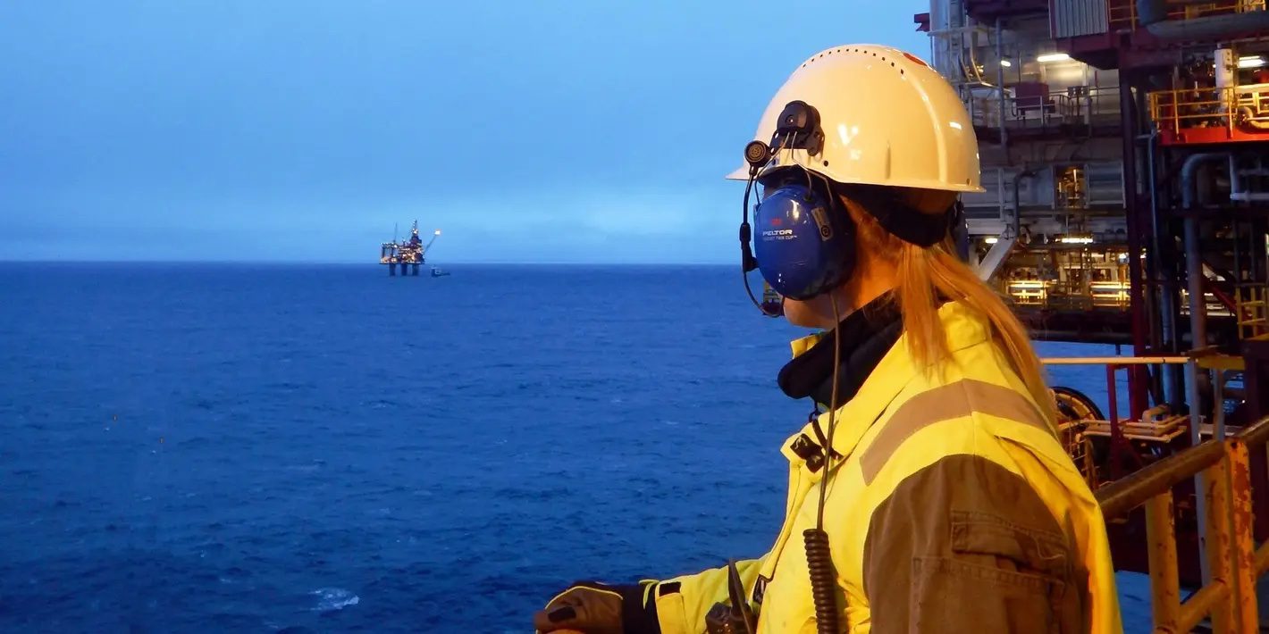offshore worker in the foreground looking out at a production platform in the background