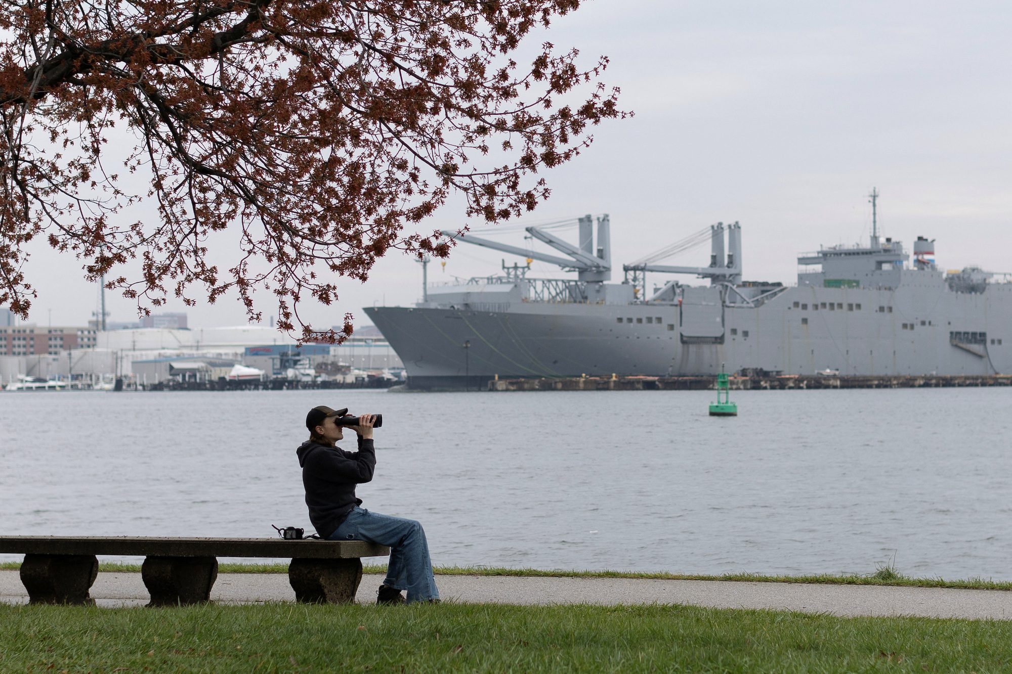Josh Ruth uses binoculars to view the Dali cargo vessel, following the collapse of the Francis Scott Key Bridge in Baltimore, Maryland, U.S., March 28, 2024. In the background is what appears to be one of the two Algol-class fast sealift vessels. REUTERS/Tom Brenner