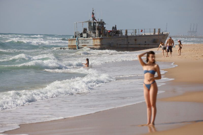 Beachgoers enjoy the windy weather as U.S. troops work on a beached vessel, used for delivering aid to Palestinians via a new U.S.-built pier in Gaza, after it got stuck trying to help another vessel behind it, on the Mediterranean coast in Ashdod, Israel May 25, 2024. REUTERS/Amir Cohen