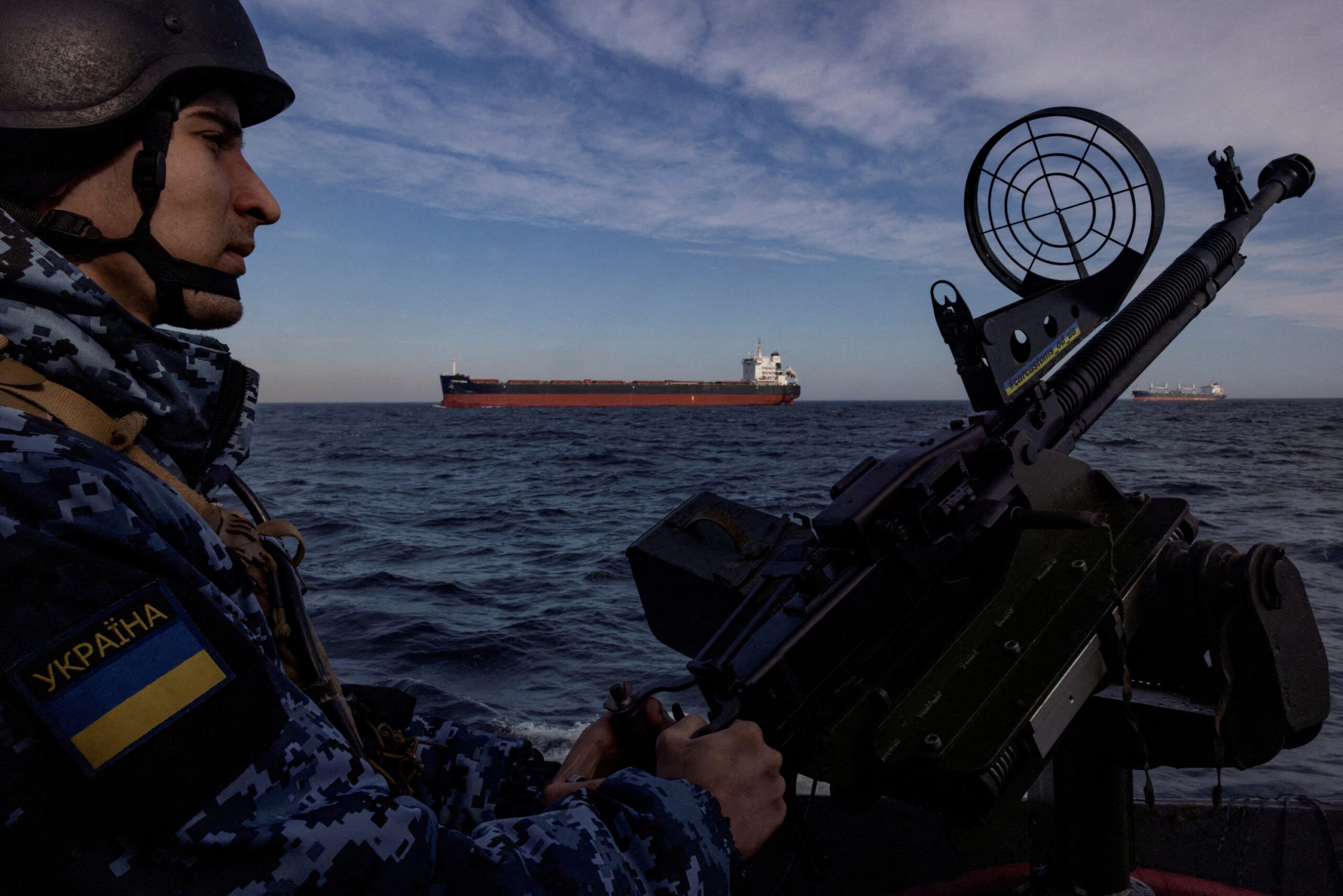 Ukraine coast guardsman manning a deck gun with an oil tanker in the background