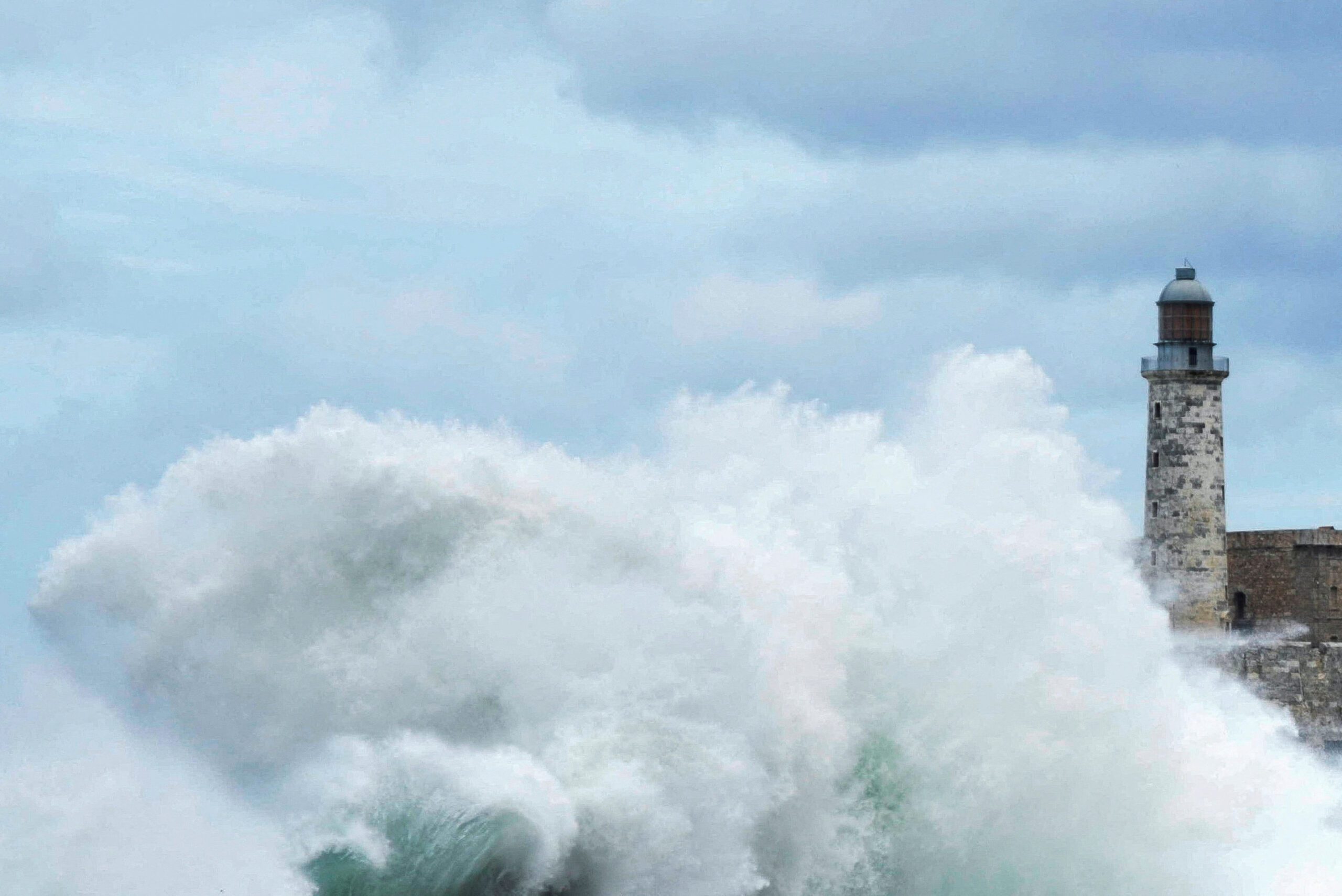 Masive hurricane wave breaks on shore with a lighthouse in the background