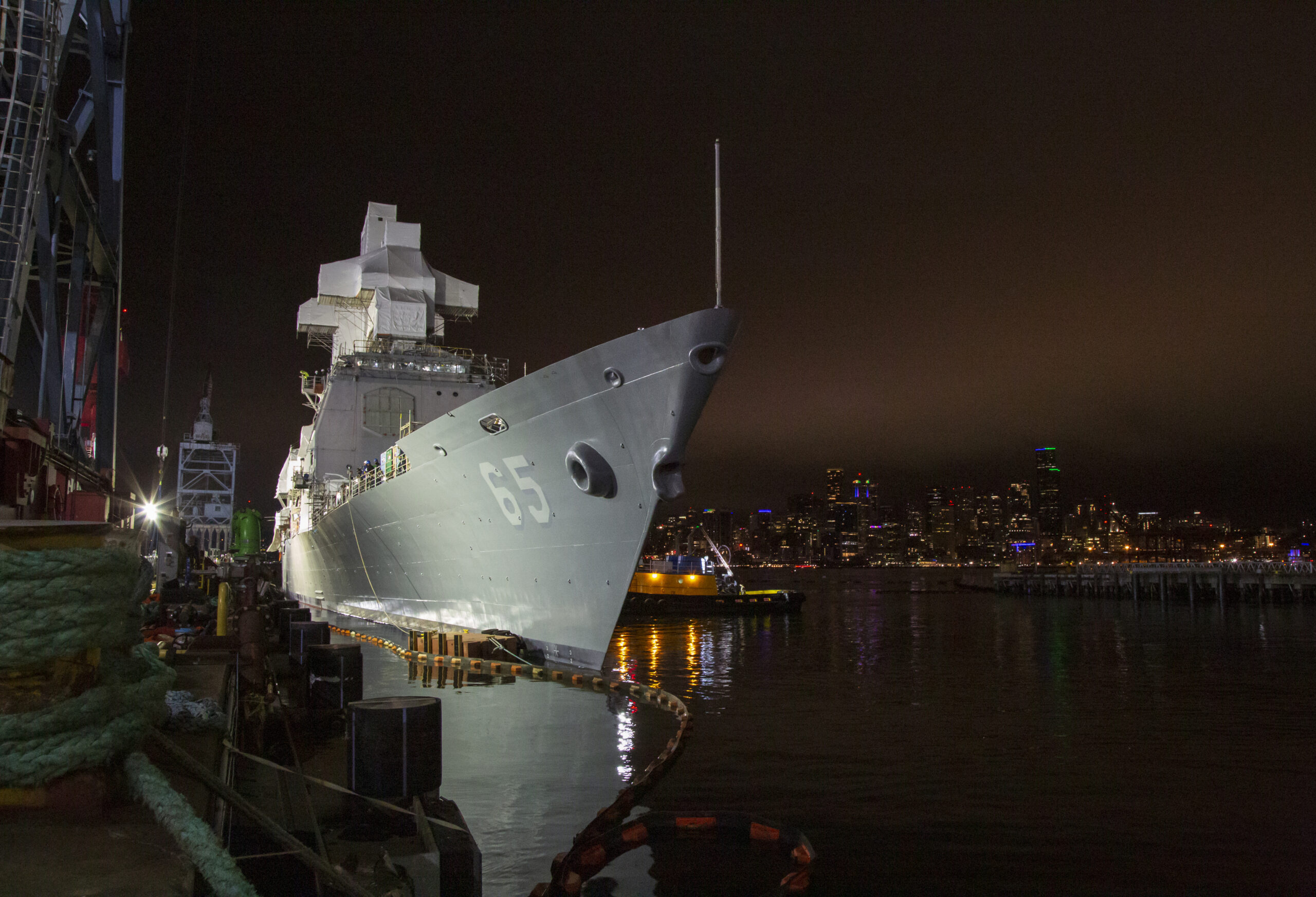 Photo of the Navy warship illuminated by lights at a dock under a dark night sky