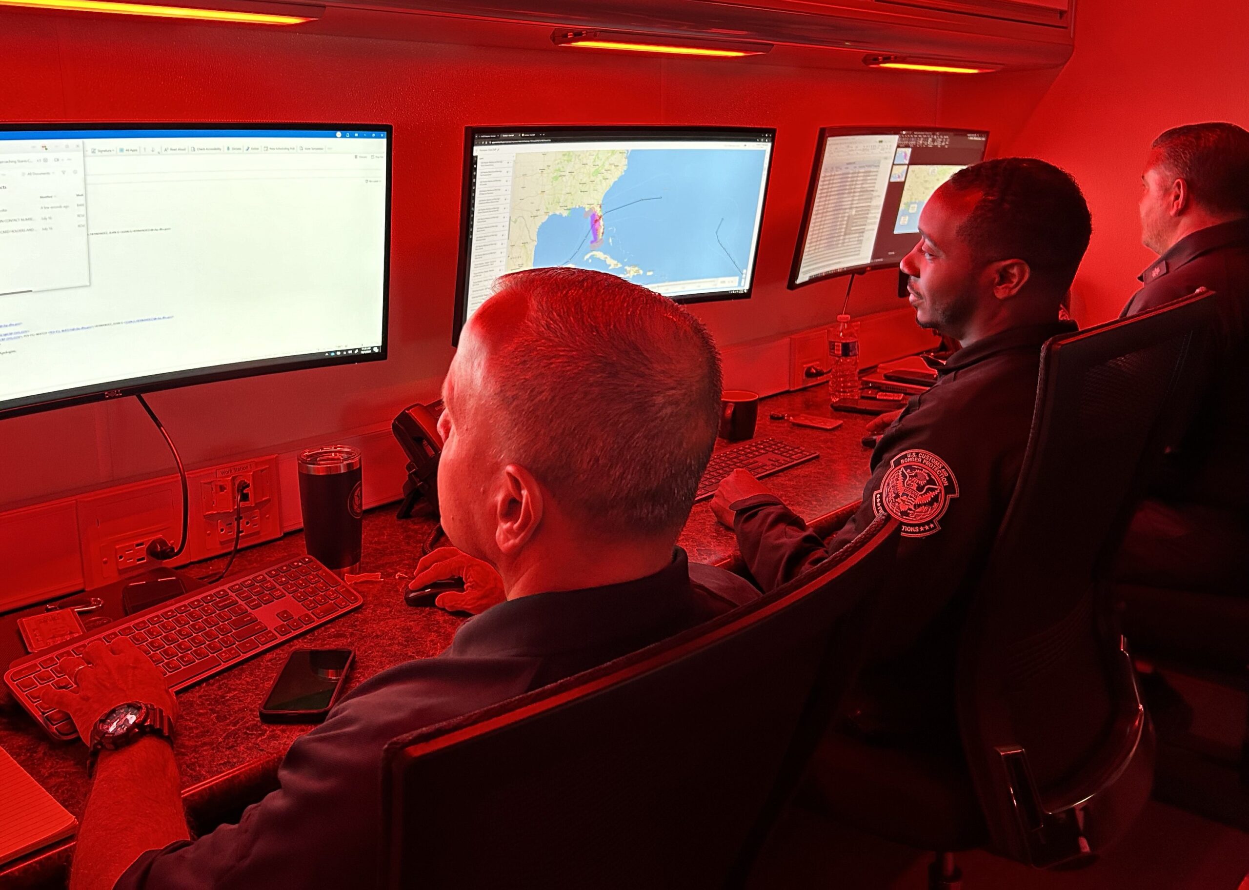 Hurricane watchstanders in room illuminated by red lights track hurricane milton on computer screens