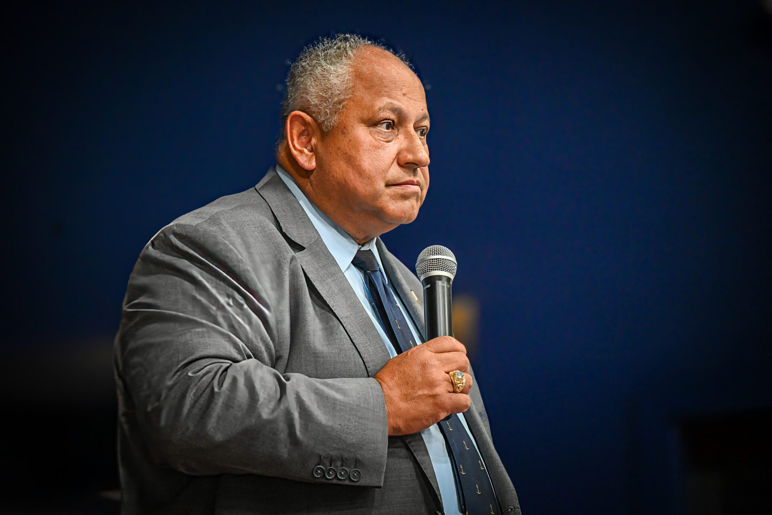 Closeup of SECNAV carlos del toro alone on stage standing with microphone