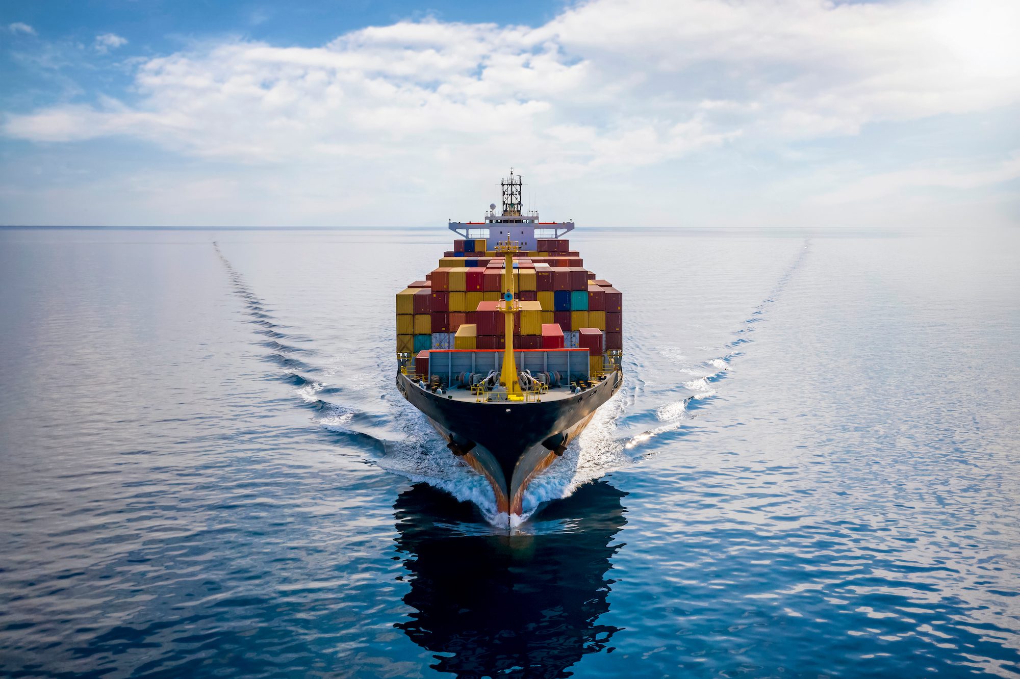 Aerial front view of a loaded container cargo vessel traveling over calm ocean