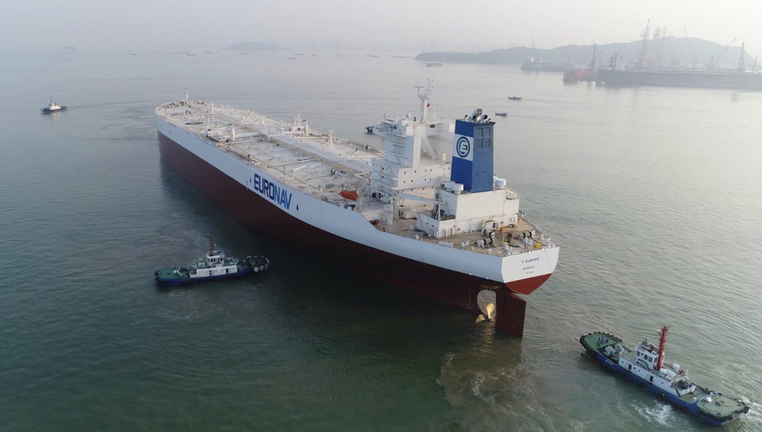 Very Large Oil Tanker painted white in port with tug-boat help