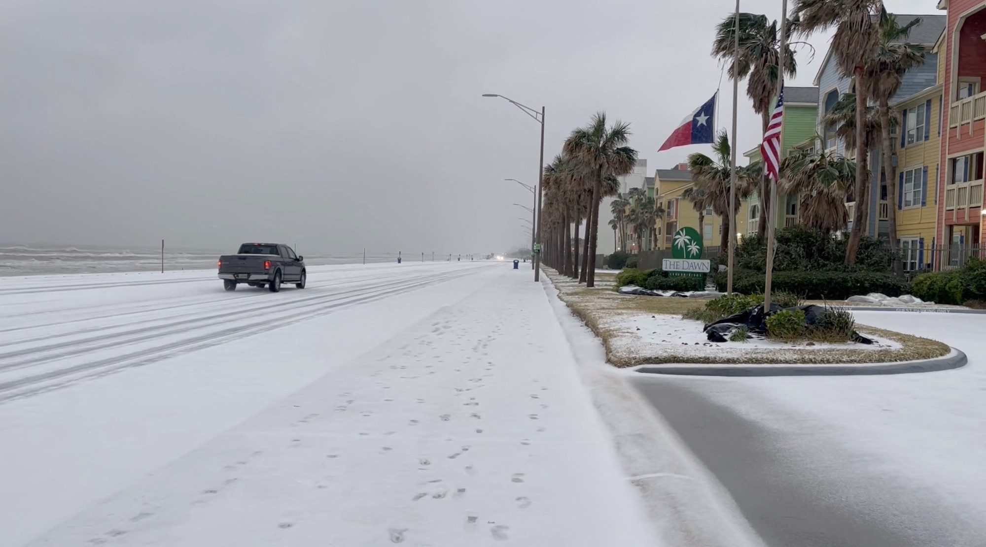 A vehicle drives on a snow-covered road by the beach following a winter storm, in Galveston, Texas