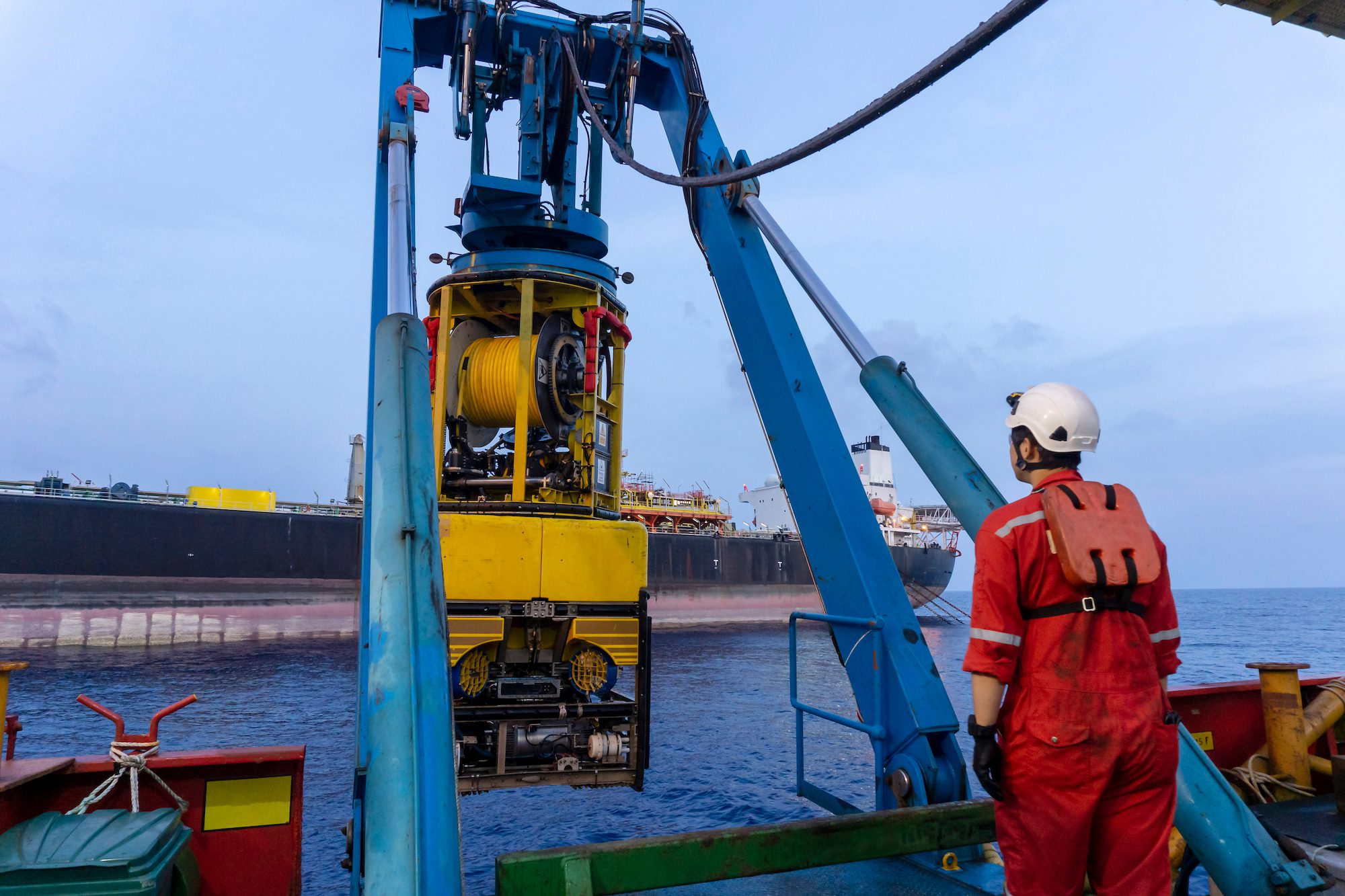 A techinician standing nearby Remoted Operated Vehicle (ROV) hanging on Launch & Recovery System (LARS) for underwater surveys