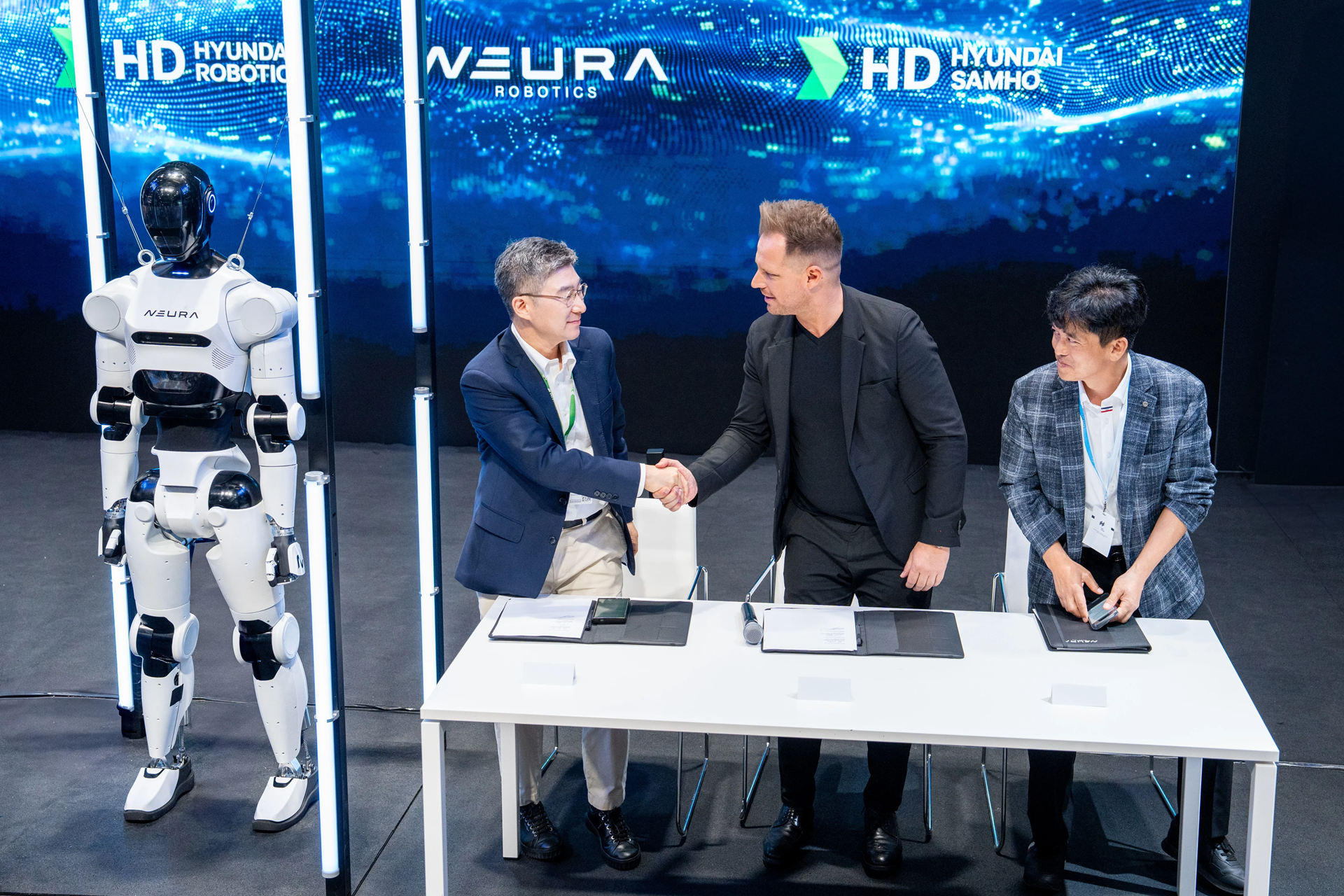 Younghoon Song, Executive Director of HD Hyundai Robotics and David Reger, Founder and CEO of NEURA Robotics shake hands after signing the agreement during Automatica in Munich, Germany at the end of June.