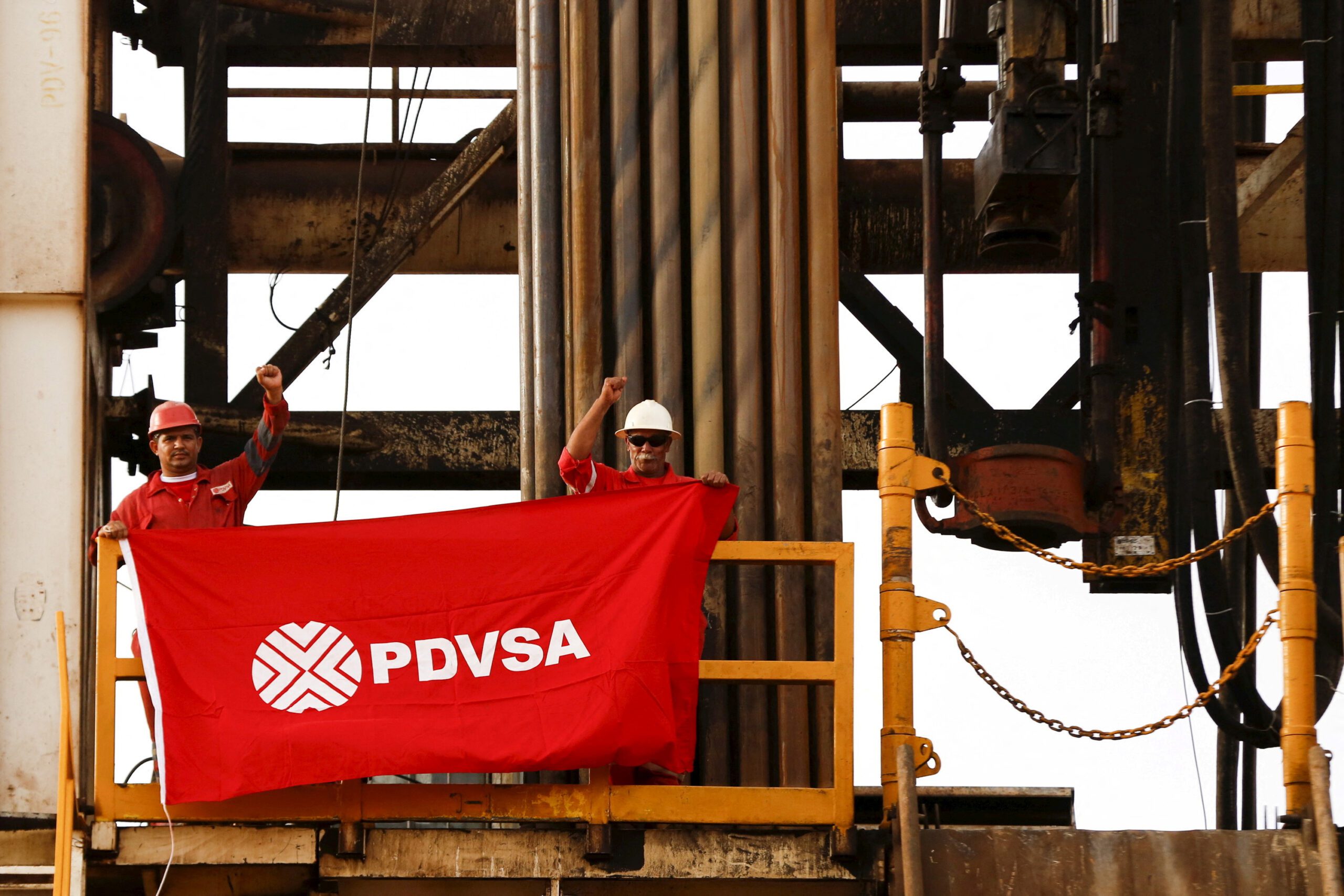 Oilfield workers hold a flag with the corporate logo of Venezuela's state oil company PDVSA, in a drilling rig at an oil well operated by them, in the oil rich Orinoco belt, near Cabrutica at the state of Anzoategui