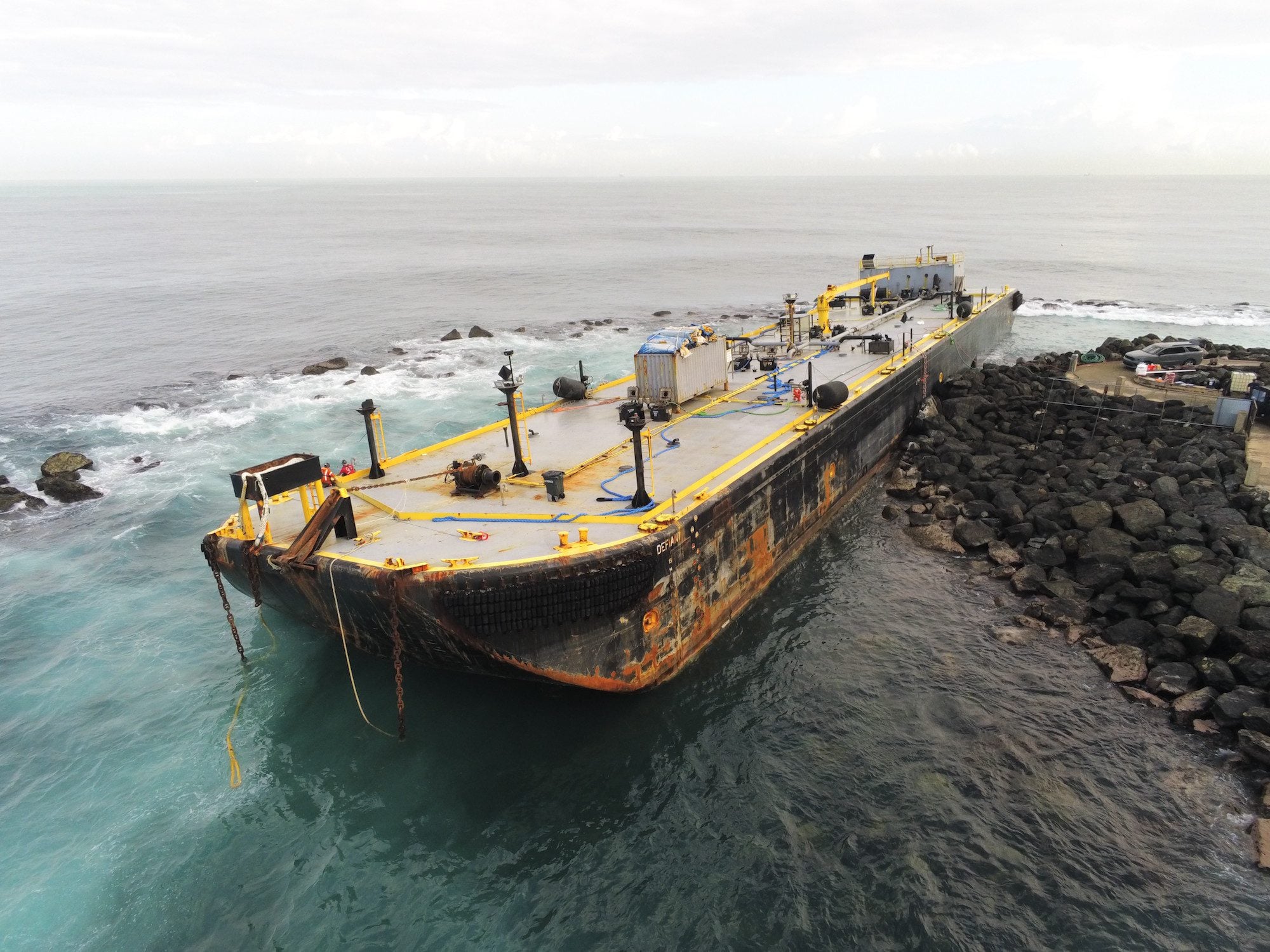 Aerial view of the 265-foot fuel barge Defiant grounded on rocks near the entrance to San Juan Harbor, Puerto Rico, as salvage crews prepare the vessel for removal.