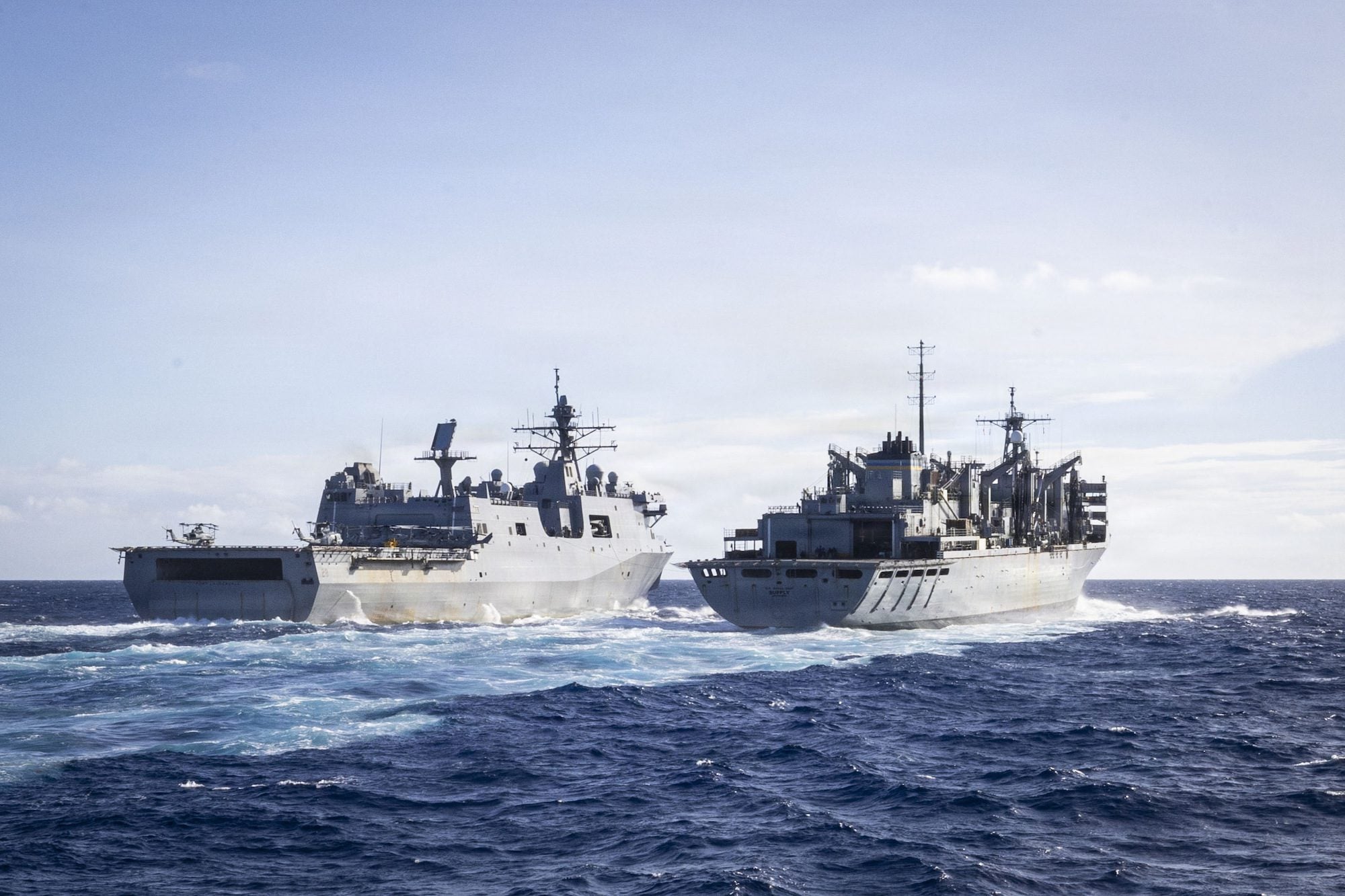 Two U.S. Navy ships conduct an underway replenishment at sea, sailing side by side in open ocean conditions.
