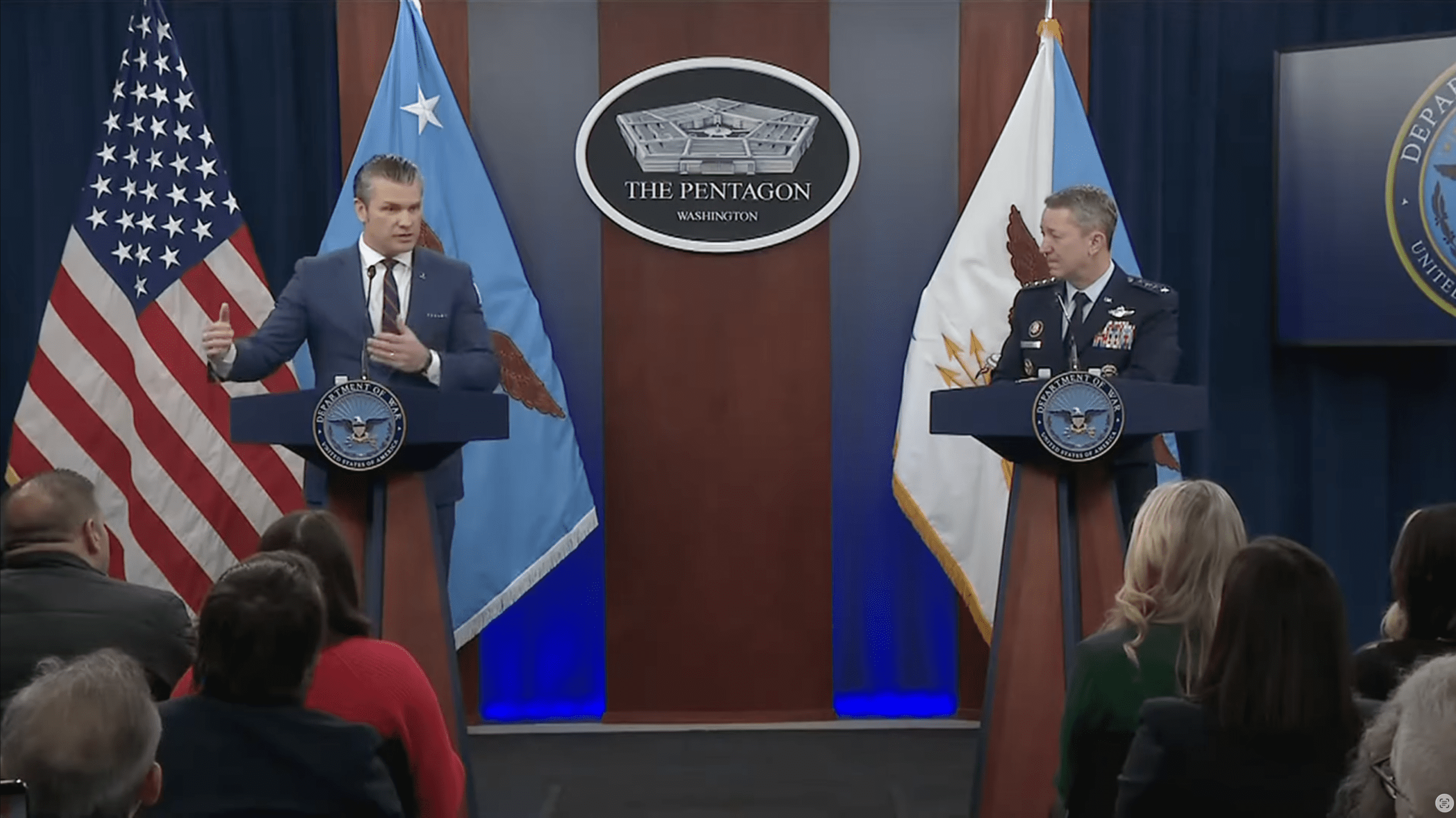 Photo of Pete Hegseth and General Daine Caine on the podium of th pentagon news breifing room