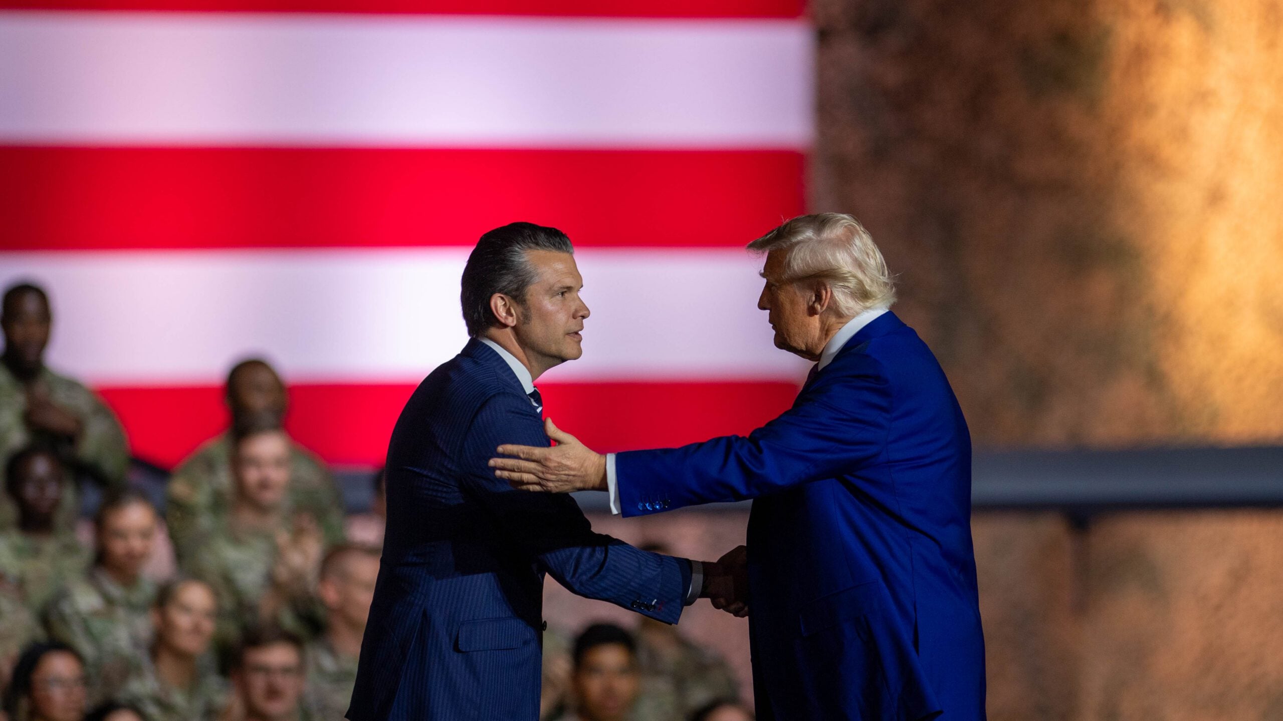 POTUS and SECWAR shaking hands under the American flag on a us military base