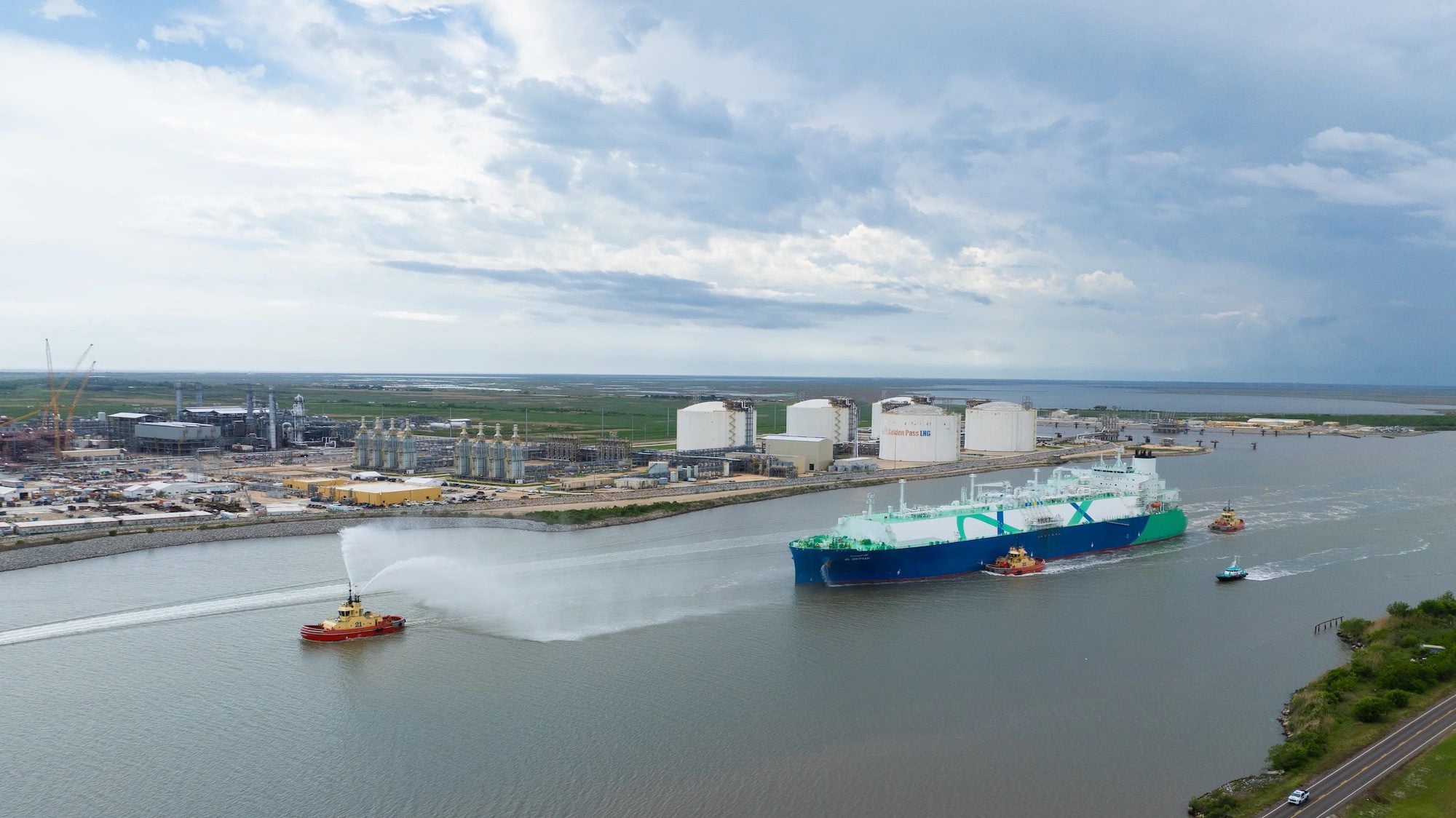 An LNG carrier departs the Golden Pass LNG terminal in Sabine Pass, Texas, escorted by tugboats in a ceremonial water salute as the project ships its inaugural export cargo