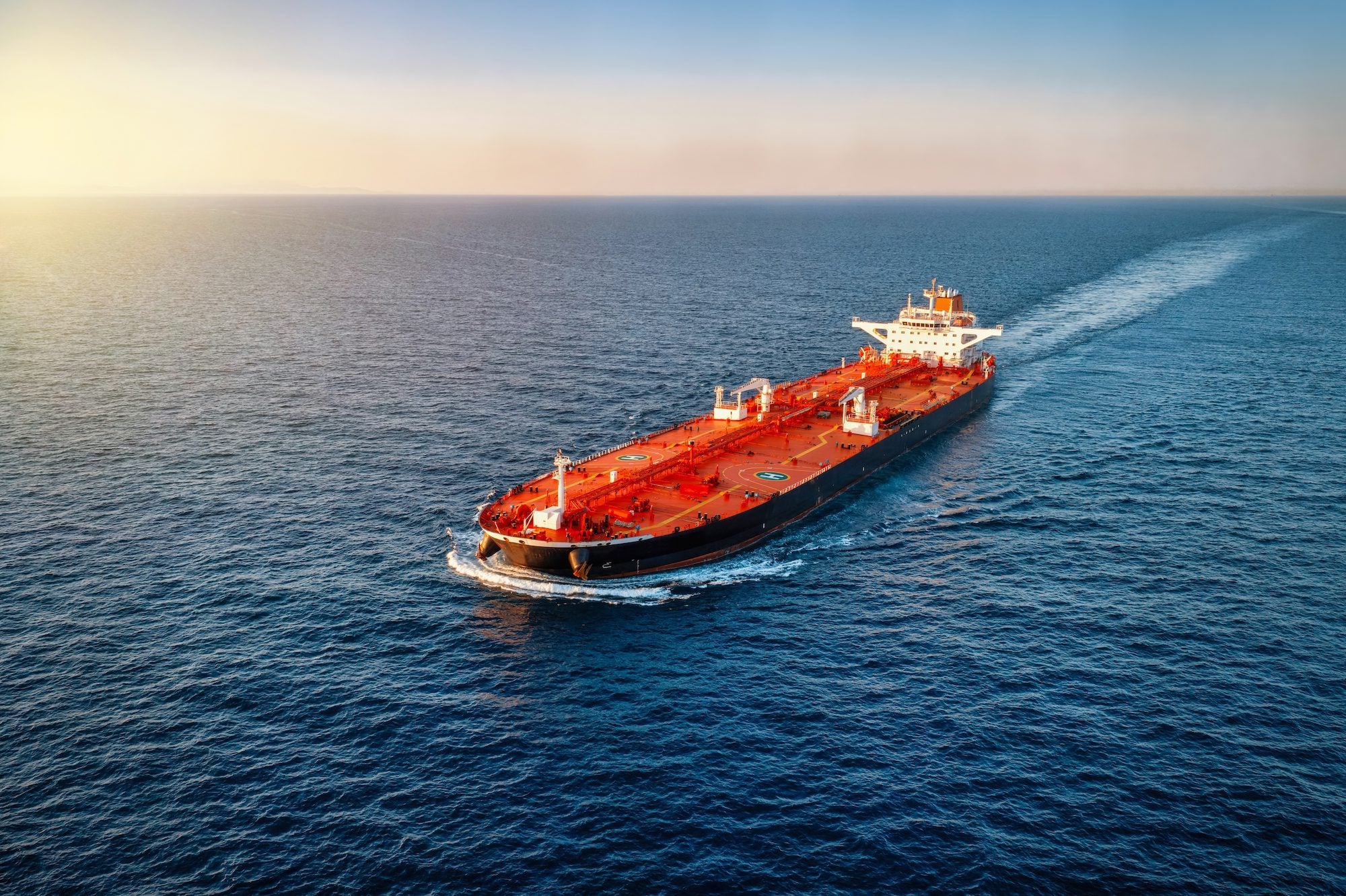Aerial view of a heavy loaded crude oil tanker traveling over open ocean during sunset time