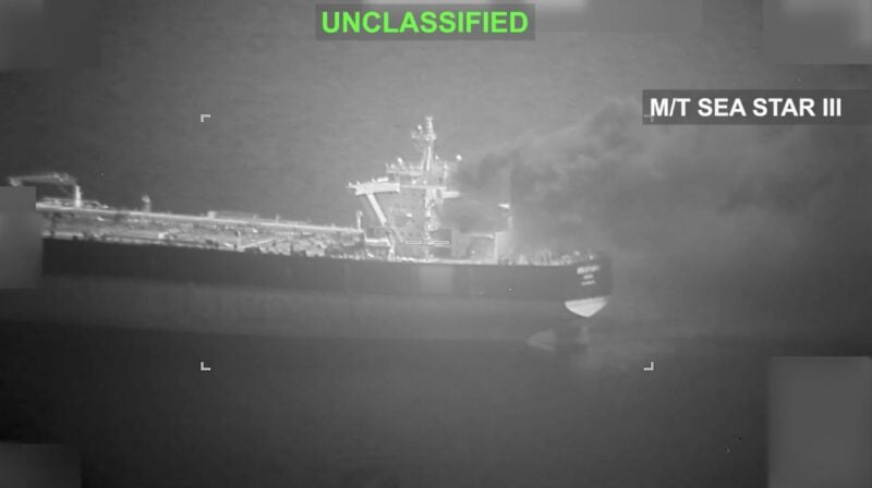 Black-and-white surveillance image labeled “UNCLASSIFIED” showing the Iranian tanker M/T Sea Star III at sea at night with smoke rising from the aft funnel area after a reported U.S. military strike during blockade enforcement operations in the Gulf of Oman.
