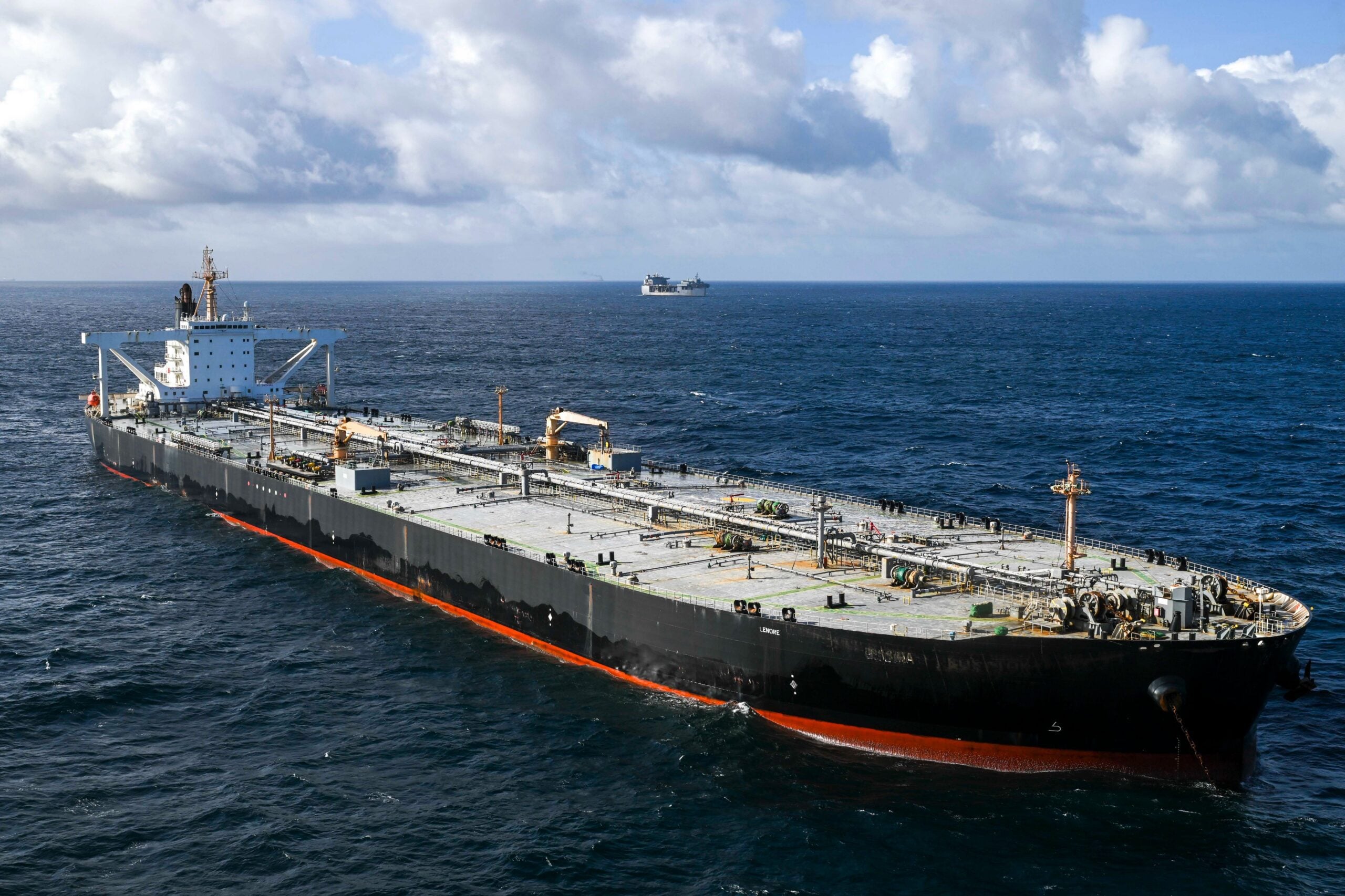 A large crude oil tanker identified as MT Davina sails in open ocean under partly cloudy skies. The black-hulled vessel is viewed from above and ahead, with another ship visible on the horizon in the background.