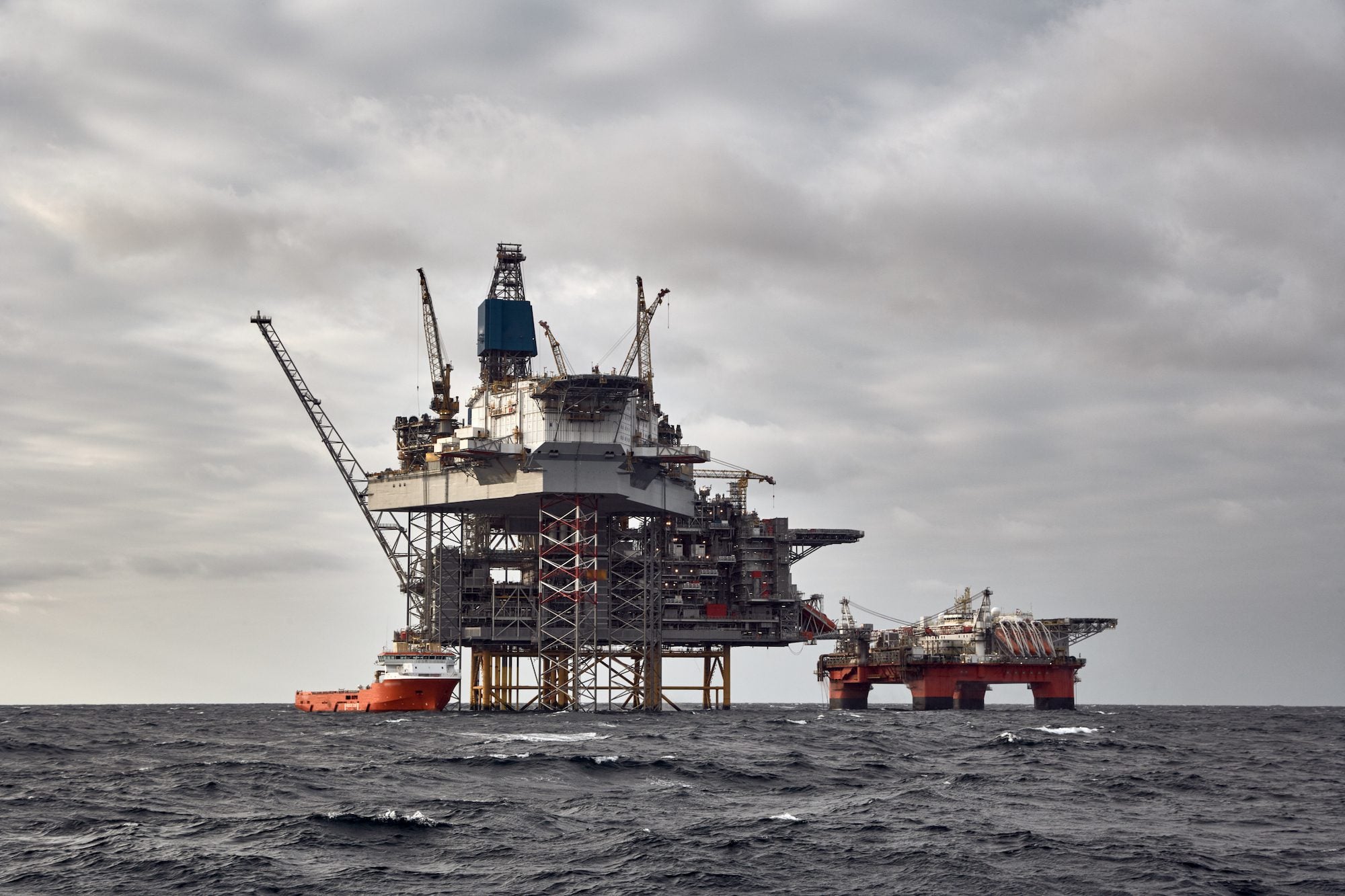 Offshore oil and gas platform with supply vessel doing cargo operations. Dark sky in the North Sea.