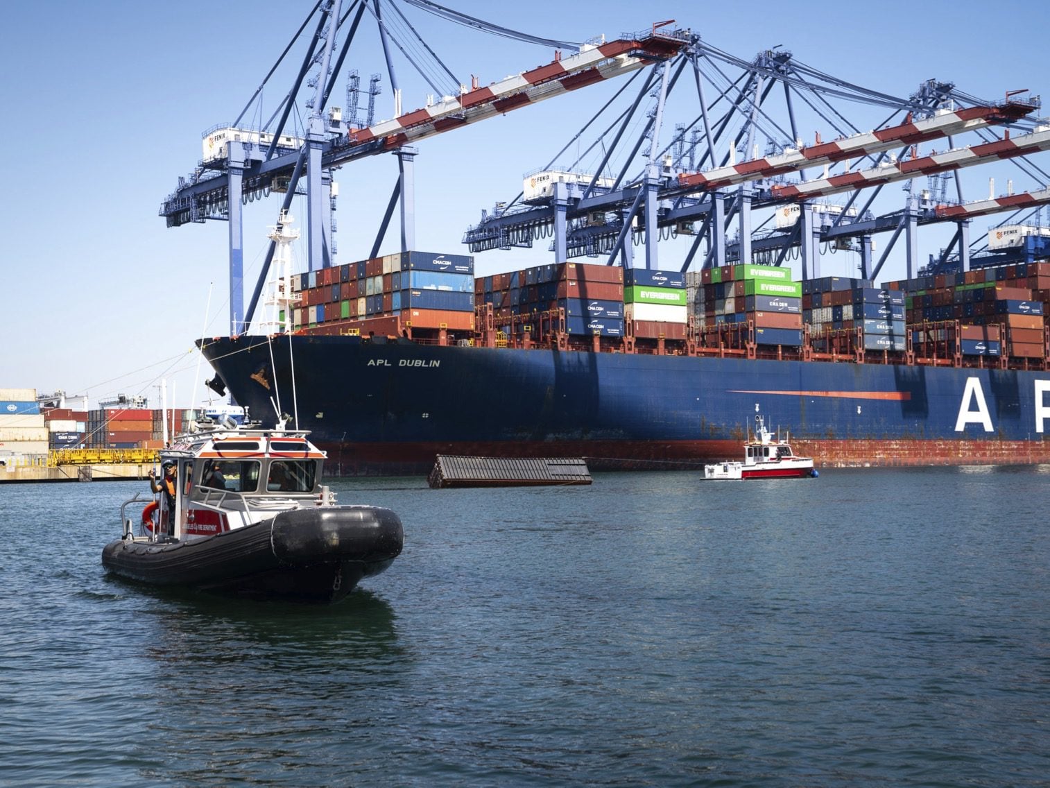 Containership APL Dublin alongside a terminal at the Port of Los Angeles with Coast Guard vessels in the foreground.