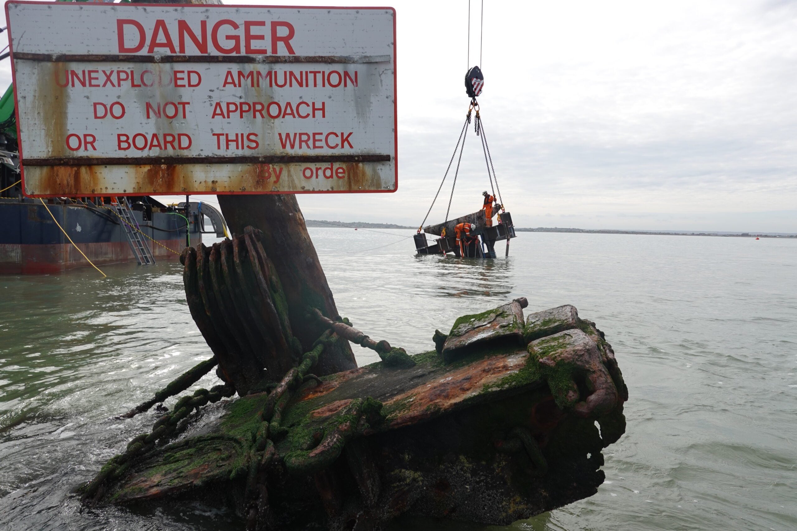 Salvage crews lift part of the SS Richard Montgomery wreck beside a warning sign reading “Danger Unexploded Ammunition” in the Thames Estuary.
